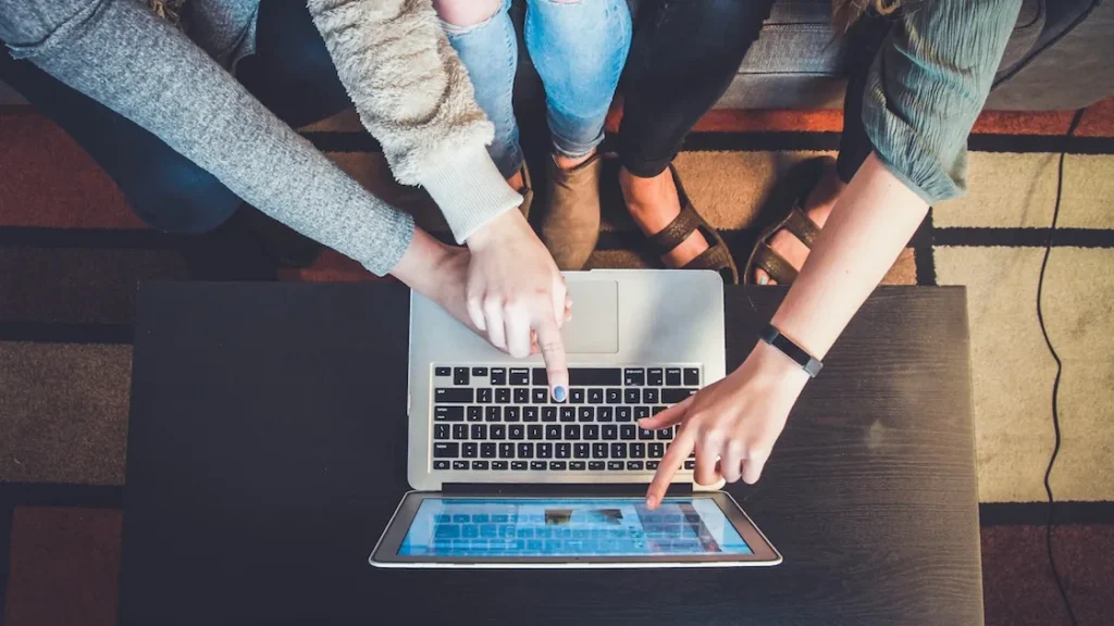 Drie mensen rond een laptop wijzen naar het scherm terwijl ze samen online browsen.